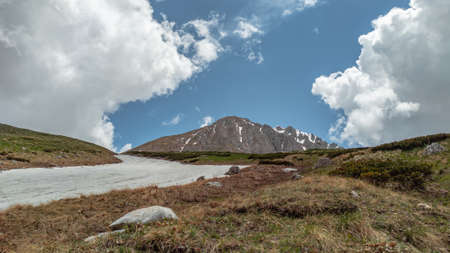 Mount Oshten against a blue sky with cumulus white clouds. The glade is partially covered with snow.の写真素材