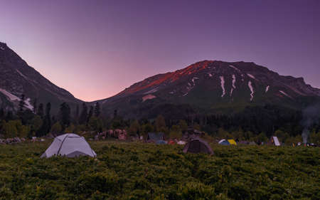 The red rays of the setting sun illuminate the top of the mountain. Tent camp in a clearing in the forest. Tourism.の写真素材