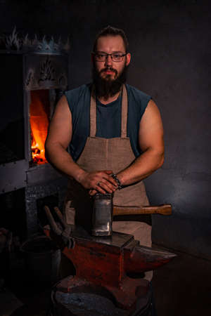 Portrait of a bearded blacksmith in the smithy. A blacksmith with poor eyesight with glasses. A...