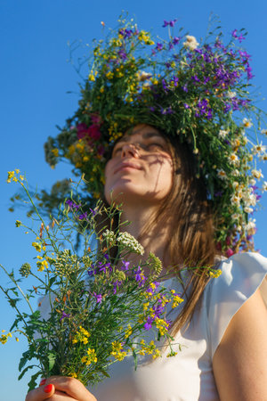 Portrait of a girl in a white dress, Slavic appearance with a bouquet and wreath of wild flowers on her head.の写真素材