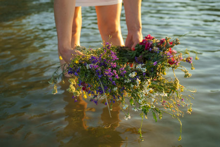 A girl lowers a wreath of wild flowers into water.の写真素材