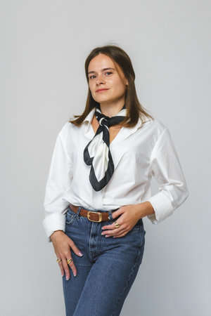 A modern businesswoman in a white shirt, blue jeans, and a scarf on a gray background. Advertising...