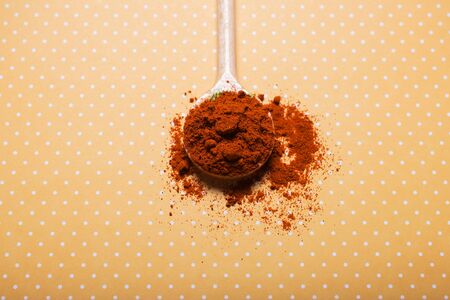 Wooden spoon with red paprika powder on plain yellow background. Top view. Minimalistic styleの写真素材