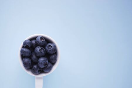 Tasty blueberries in a white cup isolated on blue. Selective focus. Text spaceの写真素材