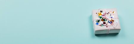 White gift box decorated with glittering metal star shaped confetti on turquoise background. Banner...