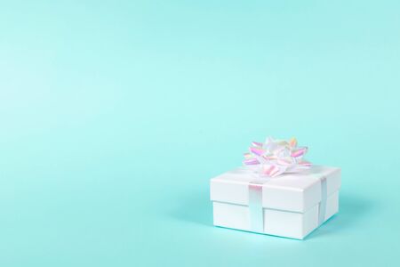 White gift box with holographic bow on pastel blue background. Shot at angle. Holiday concept. Copy space.の写真素材