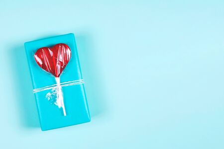 Festive background. Blue gift box decorated with red heart shaped lollipop. Flat lay style, copy spaceの写真素材