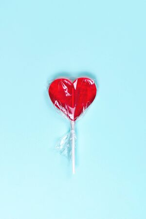 Red lollipop heart in transparent packaging on pastel blue background. Top viewの写真素材
