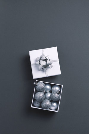 Open giftbox with silver Christmas tree metallic decorations on gray background. Top view, copy...