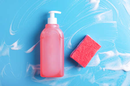 Dishwashing liquid and red sponge on foaming wet blue background. Cleaning concept.の写真素材
