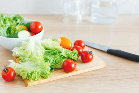 Salad preparation for lunch. Fresh vegetables, knife, cutting board, glass bowl and pure water in the background. Vibrant colors, selective focus.の写真素材