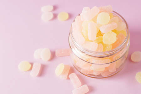 Chewing sugary citrus gummy candies in glass jar on pastel pink background. Top view, selective focus.の写真素材