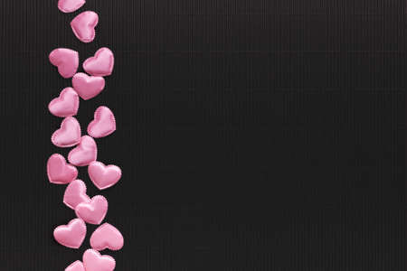 Pink silk decorative hearts scattered on black textured paper. Copy space. Valentines day romantic dark background.の写真素材