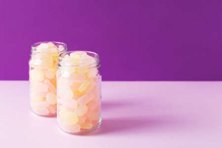Close-up of two glass jars full of citrus gummy candies on purple background. Studio shot, selective focus, room for text.の写真素材
