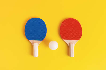 A pair of blue and red table tennis rackets and white ball on yellow background. Above view, studio shot.の写真素材