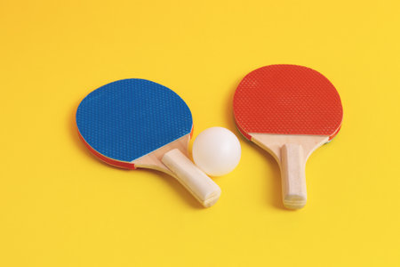 Table tennis rackets and white ball on yellow background. Sport equipment.の写真素材