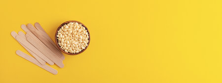 Hair removal film wax and wooden spatulas on yellow background. Depilation, beauty treatment. Banner 16:6.の写真素材