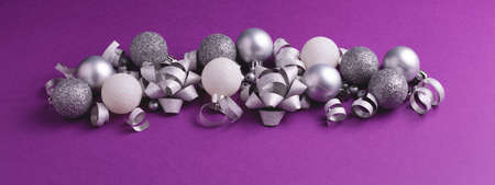 Christmas and New Year ornament on purple background. Silver and white metallic baubles and bows. Banner 16:6の写真素材