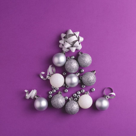 Christmas tree made of silver and white Christmas decorations on purple background. Top view. Square card.の写真素材