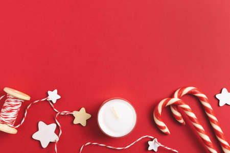Christmas ornament on red background with blank space. Holiday layout with candy cane, candle, stars and reel of string.の写真素材