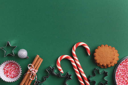 Green Christmas baking background with ginger cookies, sprinkles, candy canes, cinnamon sticks, cookie cutters and silver bauble. Xmas colors, flat lay.の写真素材