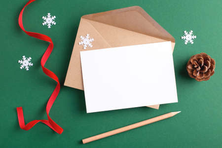 Seasons greeting mockup with blank card, kraft envelope, wooden pencil and Christmas decoration on green background.の写真素材