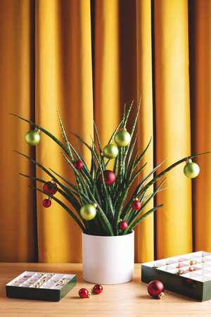 House plant decorated with Christmas toys against yellow curtains. Bright positive Holiday and New Year composition.の写真素材
