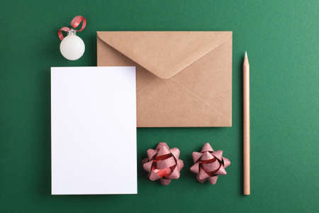 Christmas greeting mock-up with blank card, envelope, pencil and holiday decorations on green background. Top view, empty space for text.の写真素材