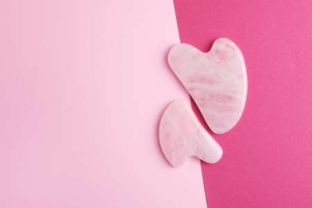 Rose quartz gua sha stones on two color pink background. Top view, copy space.の写真素材