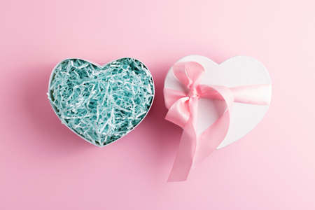 Festive heart shaped open gift box with shred paper on pastel pink background. Present concept.の写真素材