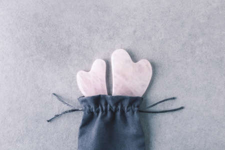 Home gua sha massage tools for natural lifting. Face and body rose quartz massagers in tissue bag on grey stone background.の写真素材