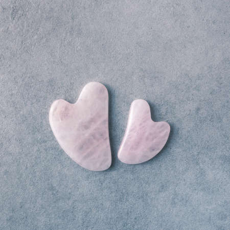 Rose quartz anti-aging massage tools on grey stone background. Pink transparent gua sha scrapers, top view.の写真素材