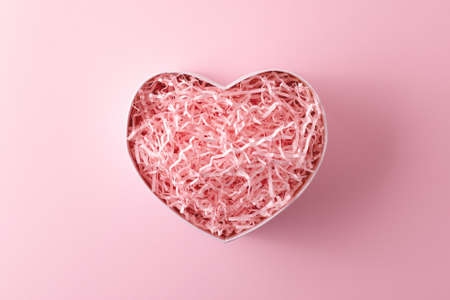 Pink heart shape made of present box with shred paper on pastel pink background. Minimalist Valentines day greeting card.の写真素材