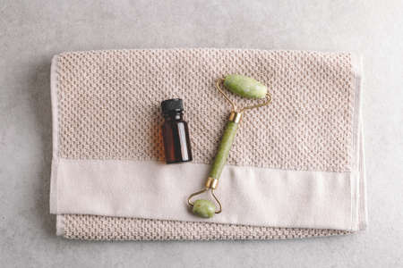 Face oil and jade sone gua sha massage roller on beige towel background. Beauty and skincare concept, flat lay.の写真素材
