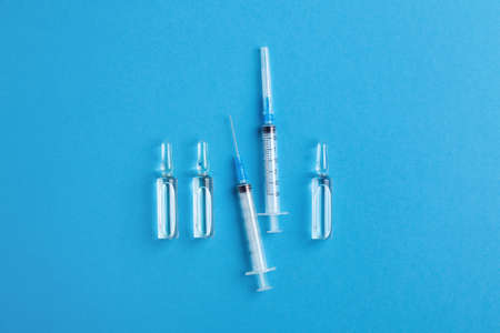 Medical glass vials and injection syringes isolated on blue background, top view. Health-care,...