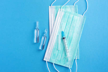 Sterile medicine background with injection ampoules, sharp needle and protective masks on clean blue...
