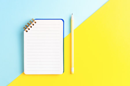 Open notebook with empty page and yellow pencil on two color blue and yellow background with blank space. Top view, business, education concept.の写真素材