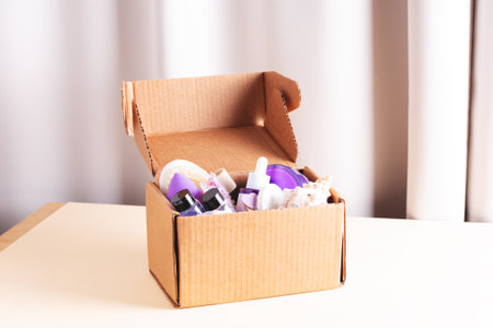 Open cardboard beauty box with various body care and skin care sample products in home interior.