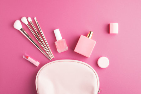 Top view of pink cosmetic bag with assorted makeup products and accessories on bright pink background. Nail polish, perfume, lipstick, cream and make-up brushes.の写真素材