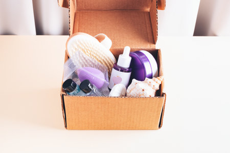 Beauty, spa, skin care products in packages in cardboard box on beige table. Cosmetic bottle with oil or serum, facial mask, shampoo, body soap, massage brush and sea decoration.の写真素材