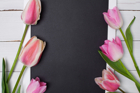 Pink tulips and chalkboard frame on the white wooden board. Top view. Valentines day card or template for your design.の写真素材
