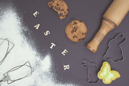 Easter day background. Flour, baked cookies and kitchen utensils on dark table. Wooden letters.の写真素材