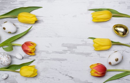 Easter eggs and tulips over wooden background.