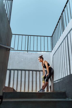 Young, fit and sporty brunette girl in sportswear. A tired athlete leaned against a concrete wall.の写真素材