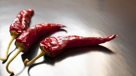 Three dried red chilli on a grey background.