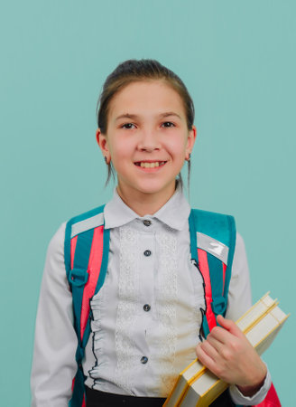 Young girl with a backpack on her back, isolated on a blue background, holding books in her hands. Distance learning at school.の写真素材