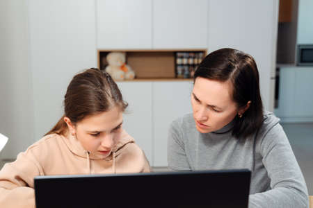 A happy family. Girl and mother are doing homework while sitting at a laptop in the room. Mom...