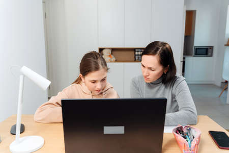A happy family. Girl and mother are doing homework while sitting at a laptop in the room. Mom...