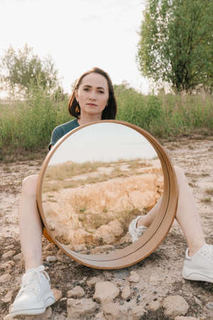 On a summer day, a girl sits with a large round mirror.の写真素材
