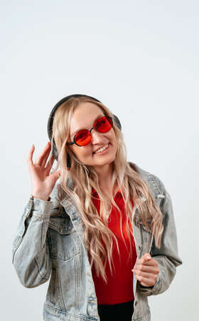 Blonde in headphones on a white background. She is wearing a denim jacket and red glasses.の写真素材